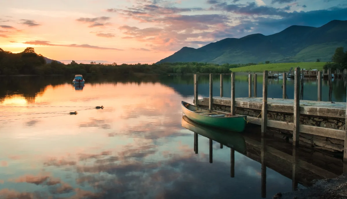 A boat beside a wooden landing stage on a lake at sunset, with mountains beyond
